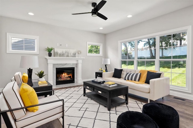 living room featuring ceiling fan, a premium fireplace, a healthy amount of sunlight, and light hardwood / wood-style floors