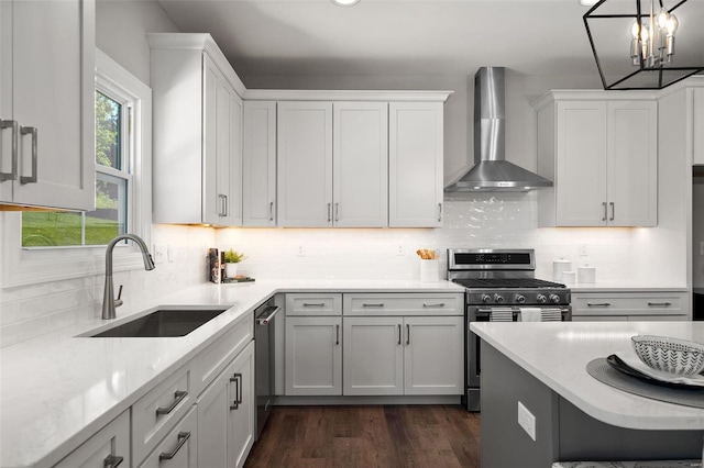 kitchen with pendant lighting, wall chimney range hood, white cabinets, appliances with stainless steel finishes, and sink