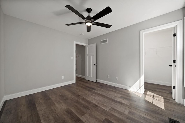 unfurnished bedroom featuring ceiling fan, a walk in closet, a closet, and dark hardwood / wood-style floors