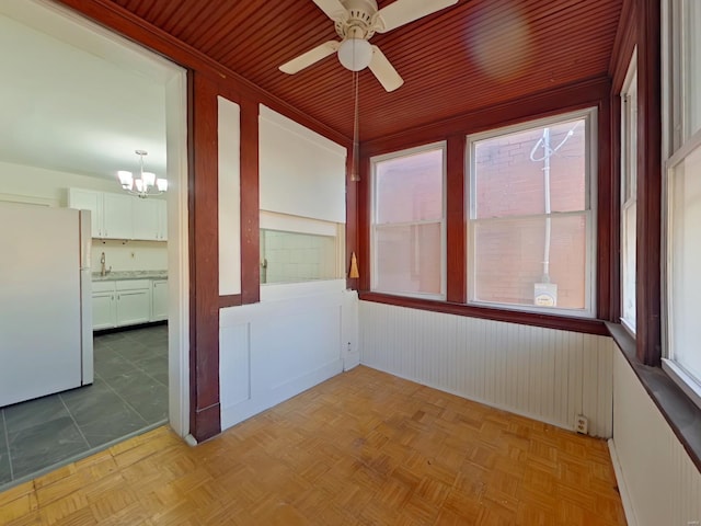 unfurnished sunroom featuring ceiling fan with notable chandelier