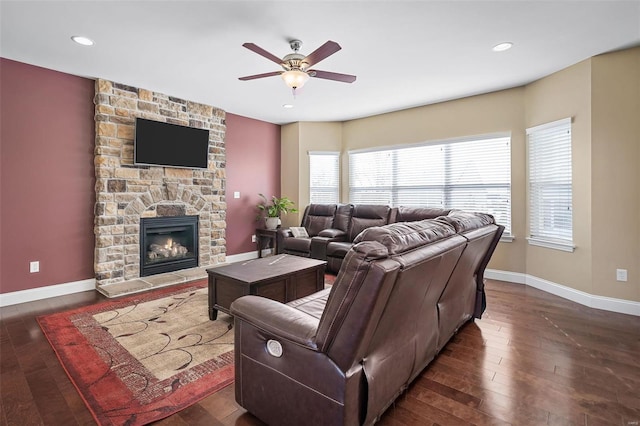 living room with a stone fireplace, ceiling fan, a healthy amount of sunlight, and dark wood-type flooring