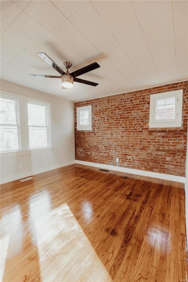 unfurnished room with ceiling fan, brick wall, and light wood-type flooring