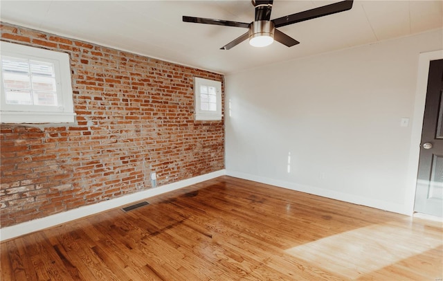 spare room featuring ceiling fan, brick wall, and wood-type flooring