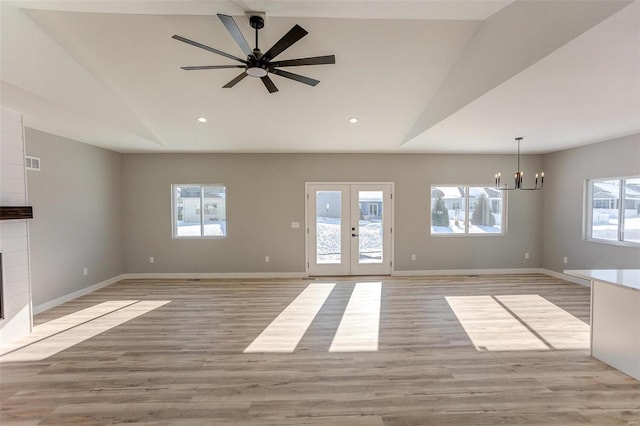 unfurnished living room featuring ceiling fan with notable chandelier, vaulted ceiling, french doors, and light hardwood / wood-style flooring