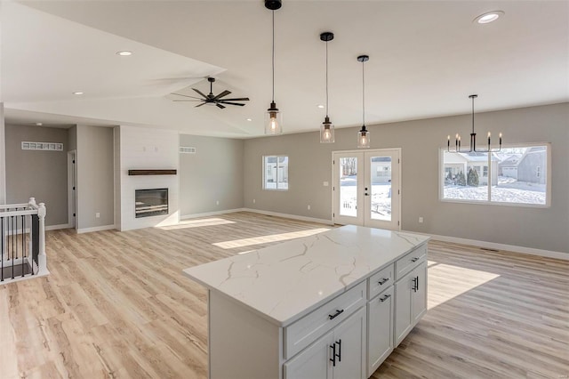 kitchen featuring a large fireplace, a kitchen island, light stone counters, decorative light fixtures, and white cabinets