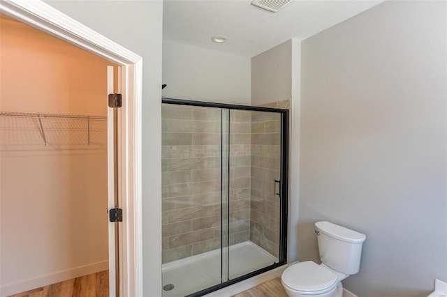 bathroom with hardwood / wood-style floors, toilet, and a shower with door