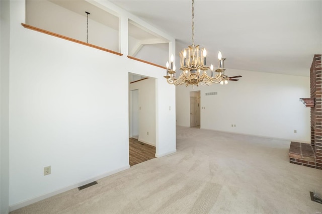 unfurnished dining area with ceiling fan with notable chandelier, high vaulted ceiling, a brick fireplace, and carpet floors