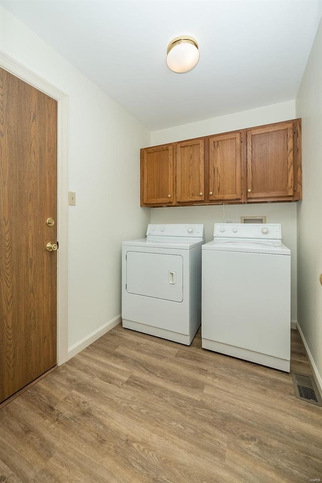 laundry area with cabinets, washing machine and clothes dryer, and light hardwood / wood-style floors