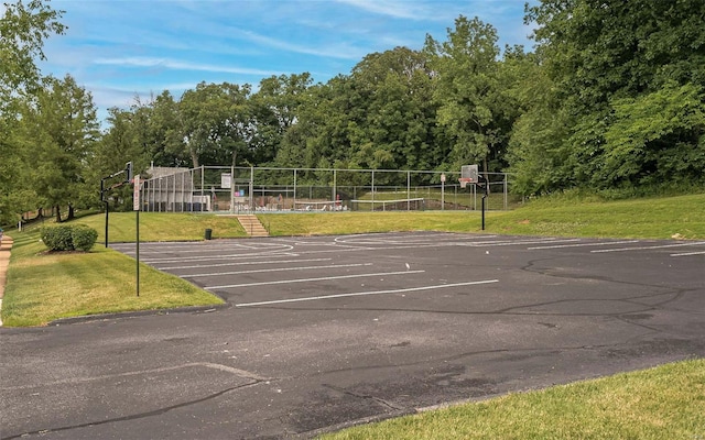 view of parking / parking lot with basketball hoop and a lawn