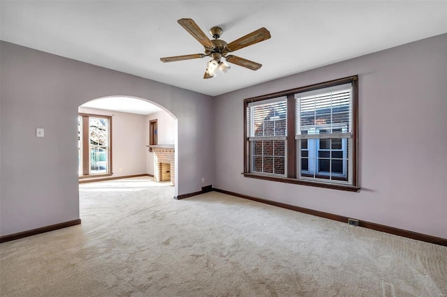 carpeted empty room featuring ceiling fan, a healthy amount of sunlight, and a brick fireplace