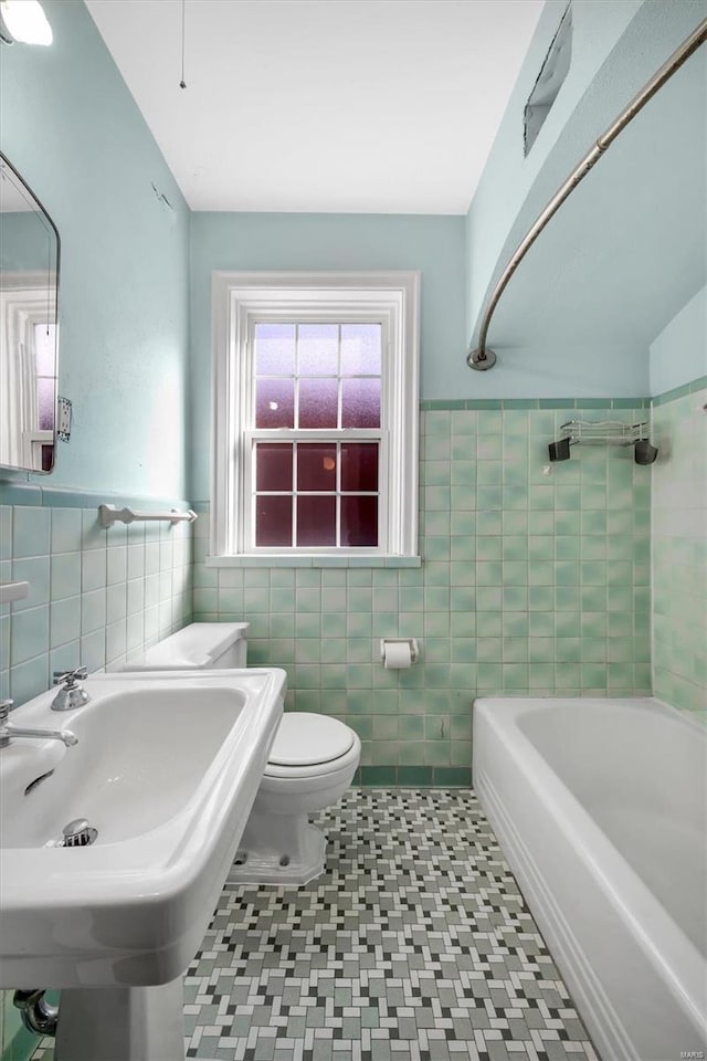 bathroom with tile walls, toilet, a bath, and tile patterned flooring