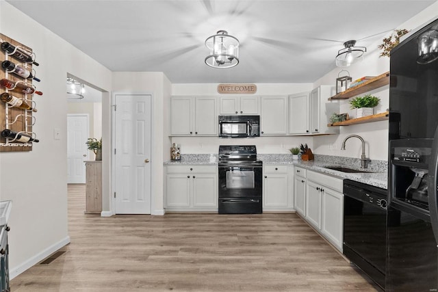 kitchen with light stone countertops, white cabinets, black appliances, sink, and light hardwood / wood-style flooring