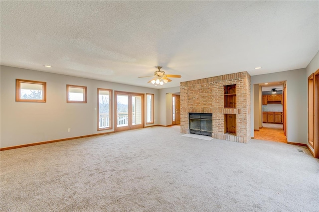 unfurnished living room featuring a fireplace, light carpet, a textured ceiling, and ceiling fan