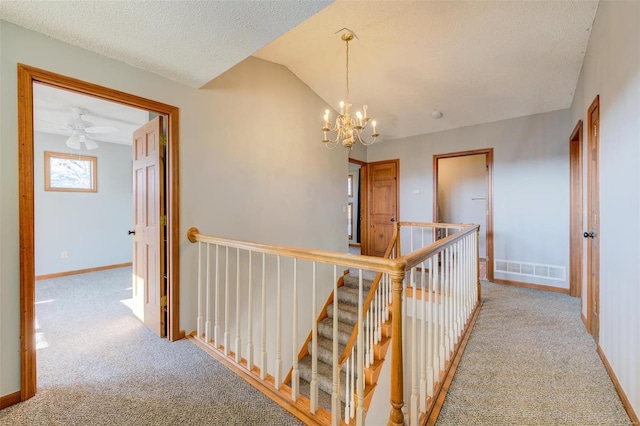 hall with a chandelier, light carpet, a textured ceiling, and vaulted ceiling