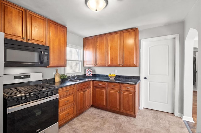 kitchen featuring sink, stainless steel range with gas stovetop, and dark stone countertops