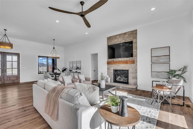 living room featuring french doors, a fireplace, light hardwood / wood-style floors, and ceiling fan with notable chandelier