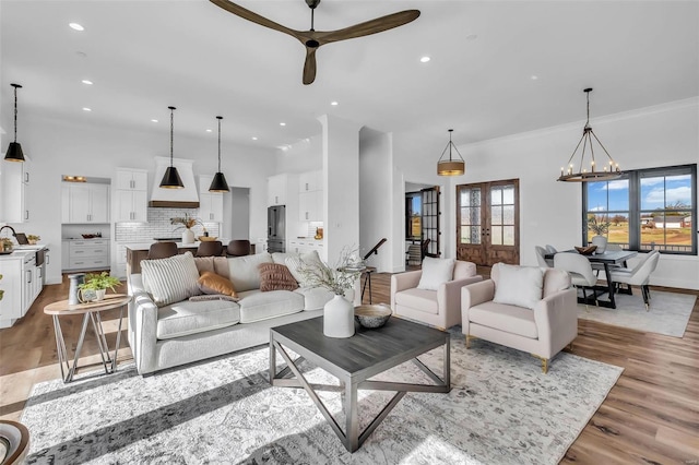 living room featuring french doors, ornamental molding, ceiling fan with notable chandelier, sink, and light hardwood / wood-style flooring