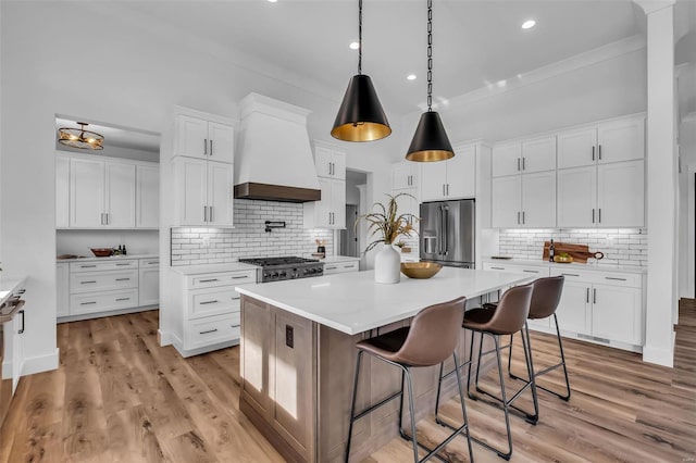 kitchen with appliances with stainless steel finishes, backsplash, custom range hood, a kitchen island, and white cabinetry