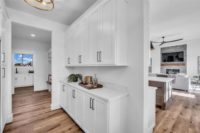 bar featuring ceiling fan, a stone fireplace, white cabinetry, and light wood-type flooring