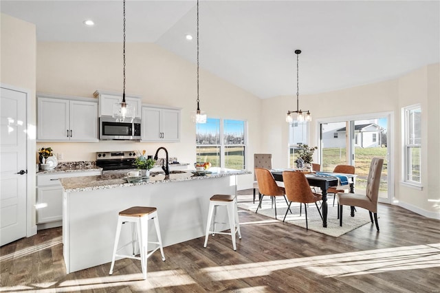 kitchen featuring light stone counters, a center island with sink, white cabinets, and stainless steel appliances