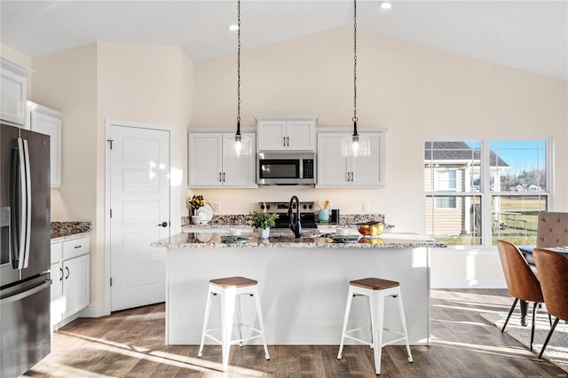 kitchen with light stone countertops, stainless steel appliances, a kitchen island with sink, pendant lighting, and white cabinets