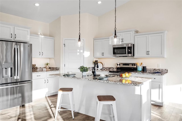 kitchen with white cabinets, light hardwood / wood-style flooring, an island with sink, light stone counters, and stainless steel appliances