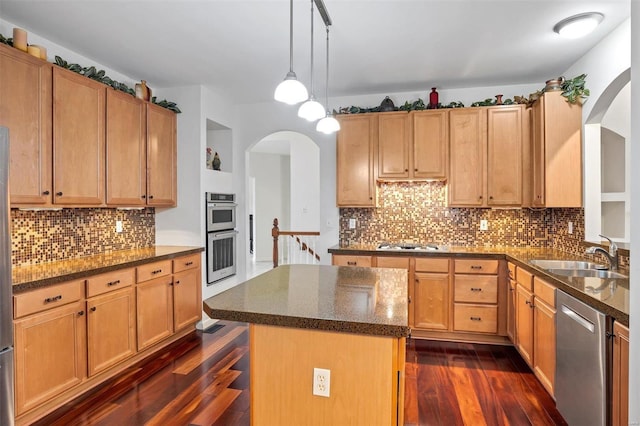 kitchen with pendant lighting, sink, appliances with stainless steel finishes, a kitchen island, and dark hardwood / wood-style flooring