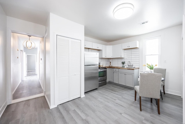 kitchen with sink, stainless steel appliances, light hardwood / wood-style flooring, butcher block countertops, and decorative backsplash