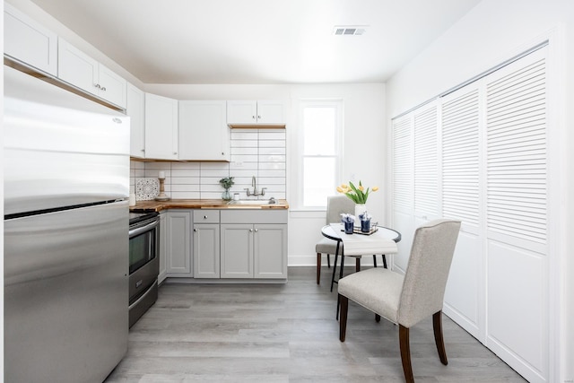 kitchen with backsplash, sink, appliances with stainless steel finishes, butcher block countertops, and white cabinetry