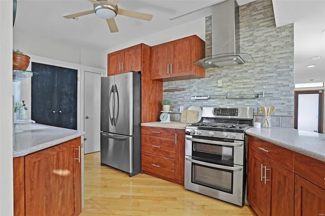 kitchen featuring sink, ceiling fan, stainless steel appliances, wall chimney range hood, and light wood-type flooring