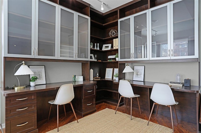 office space with wood-type flooring, built in desk, and track lighting