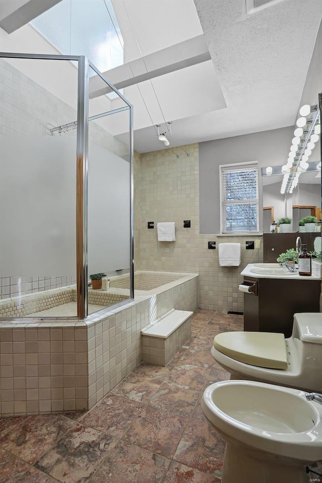 bathroom featuring a bidet, tile walls, vanity, a textured ceiling, and toilet