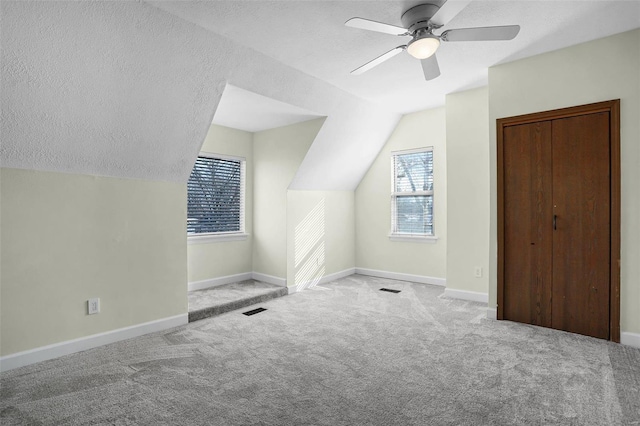 bonus room featuring vaulted ceiling, light colored carpet, ceiling fan, and a textured ceiling