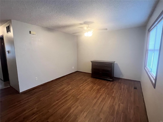 empty room with a wealth of natural light, a textured ceiling, dark hardwood / wood-style floors, and ceiling fan