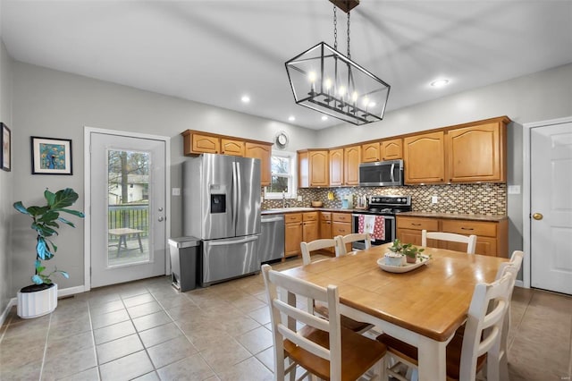 kitchen with tasteful backsplash, stainless steel appliances, pendant lighting, light tile patterned floors, and an inviting chandelier