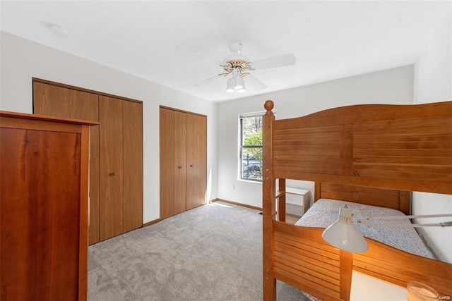 unfurnished bedroom with two closets, ceiling fan, and light carpet