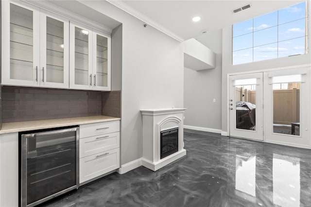 bar with white cabinetry, backsplash, wine cooler, and ornamental molding