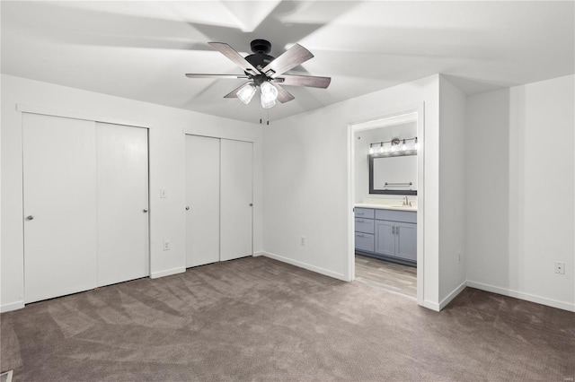 unfurnished bedroom featuring sink, ensuite bath, ceiling fan, light colored carpet, and multiple closets