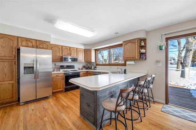 kitchen with sink, a kitchen bar, light wood-type flooring, kitchen peninsula, and appliances with stainless steel finishes