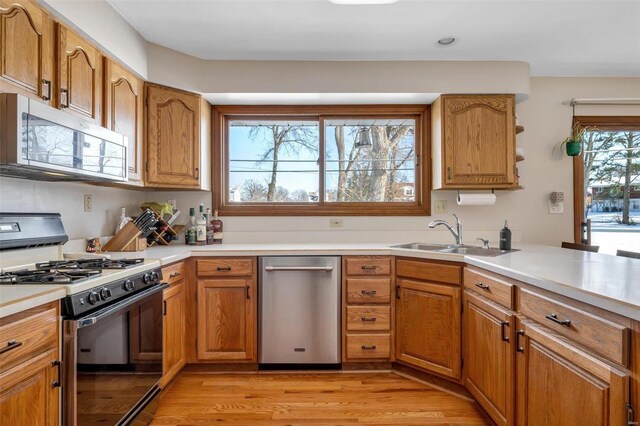 kitchen with dishwasher, light wood-type flooring, kitchen peninsula, gas range oven, and sink