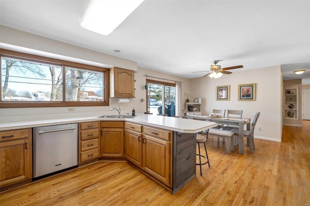 kitchen featuring light wood-type flooring, kitchen peninsula, a kitchen bar, sink, and stainless steel dishwasher