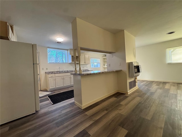 kitchen with heating unit, kitchen peninsula, light stone countertops, white refrigerator, and dark wood-type flooring