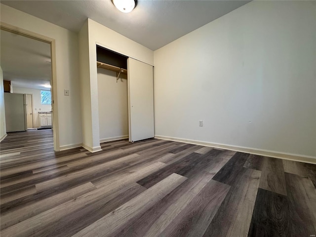 unfurnished bedroom with stainless steel refrigerator, a closet, and dark hardwood / wood-style floors