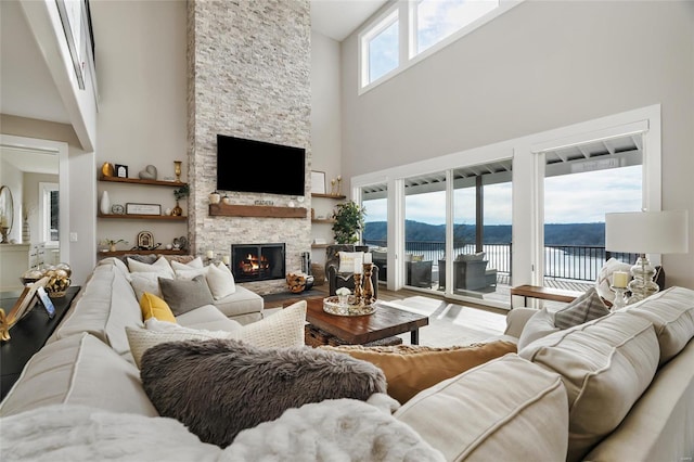 living room with hardwood / wood-style flooring, a stone fireplace, and a towering ceiling