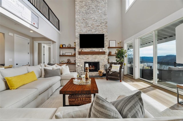 living room featuring a high ceiling, light hardwood / wood-style floors, a stone fireplace, and plenty of natural light