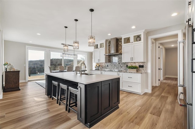 kitchen with a kitchen island with sink, hanging light fixtures, sink, wall chimney exhaust hood, and white cabinetry