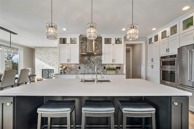 kitchen featuring backsplash, wall chimney exhaust hood, an island with sink, and stainless steel appliances