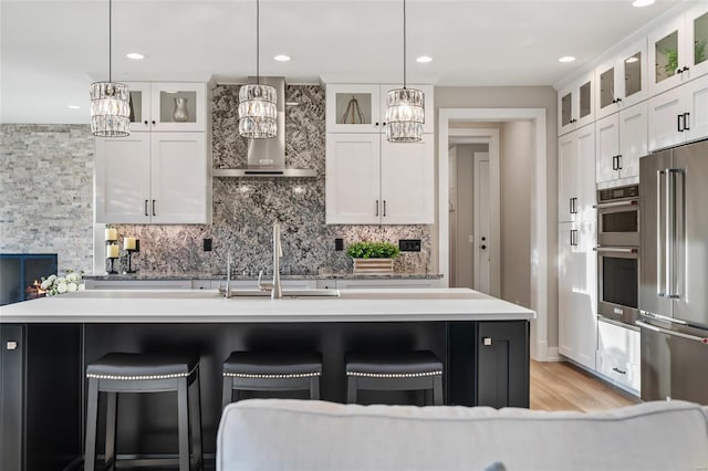 kitchen with white cabinets, wall chimney exhaust hood, stainless steel appliances, and decorative light fixtures