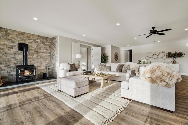 living room with a wood stove, ceiling fan, and wood-type flooring