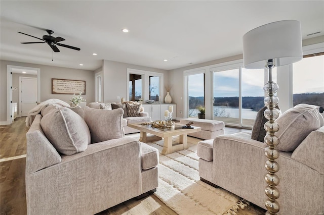 living room featuring hardwood / wood-style floors, ceiling fan, and a water view